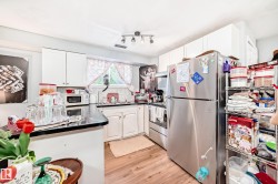 Kitchen featuring wood-finish flooring, white cabinetry, dark countertops, a tile backsplash, and a stainless steel refrigerator - 