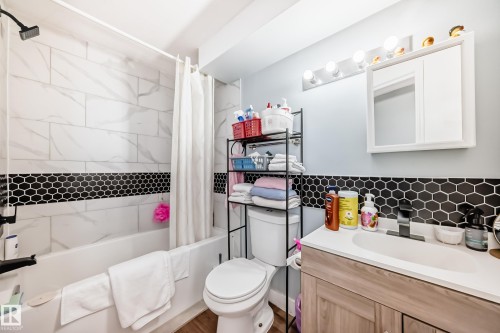 Bathroom featuring a white bathtub, subway tile surround with a black hexagon accent, a wood-finish vanity with a white countertop and integrated sink, a mirrored medicine cabinet, and a five-light vanity fixture - 10017 153 Street, Edmonton, AB - Indoor Photo Showing Bathroom