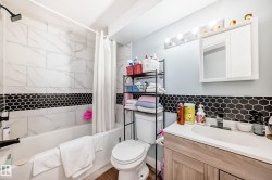 Bathroom featuring a white bathtub, subway tile surround with a black hexagon accent, a wood-finish vanity with a white countertop and integrated sink, a mirrored medicine cabinet, and a five-light vanity fixture - 