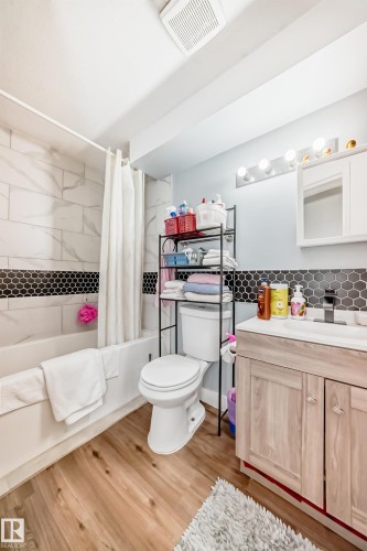 Bathroom featuring wood-finish flooring, a white bathtub with subway tile surround and black hexagonal accent tile, and a light-toned wood-finish vanity with a white countertop - 10017 153 Street, Edmonton, AB - Indoor Photo Showing Bathroom