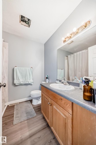 Bathroom featuring wood-finish flooring, a vanity with wood-finish cabinetry, an integrated sink, and a large wall mirror - 10017 153 Street, Edmonton, AB - Indoor Photo Showing Bathroom