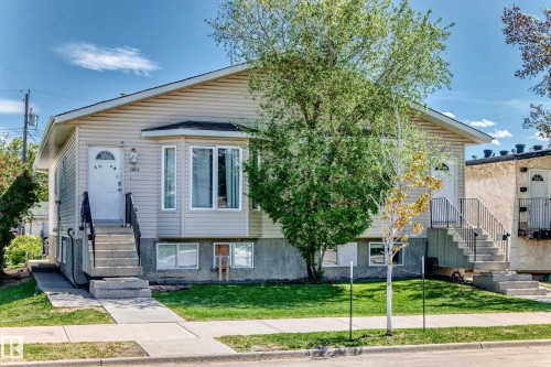 Duplex exterior featuring light-toned siding, a prominent bay window, and concrete entry stairs with black metal railings - 10017 153 Street, Edmonton, AB - Outdoor With Facade