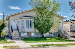 Duplex exterior featuring light-toned siding, a prominent bay window, and concrete entry stairs with black metal railings - 