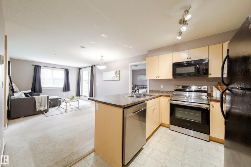 Open-concept living space featuring a kitchen with light wood-finish cabinetry and stainless steel appliances, a breakfast bar, and a living area with carpet flooring and a balcony access point - 115 4309 33 Street, Stony Plain, AB 