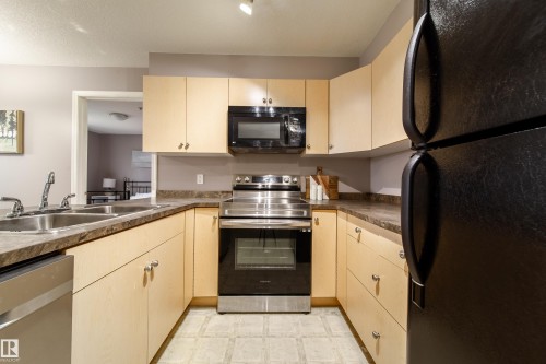 U-shaped kitchen featuring light wood cabinetry, stone-look countertops, stainless steel appliances, and tile flooring - 115 4309 33 Street, Stony Plain, AB 