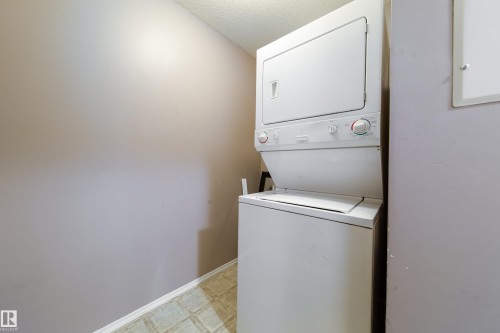 Dedicated laundry space featuring a stacked white washer and dryer unit, neutral wall color, and patterned floor tiling - 115 4309 33 Street, Stony Plain, AB 