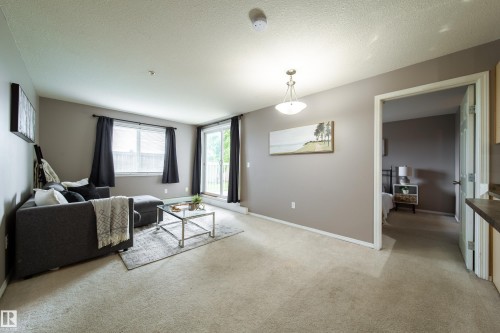 Carpeted living area featuring a sliding glass door to exterior, a window with blinds, and a permanent ceiling fixture - 115 4309 33 Street, Stony Plain, AB 