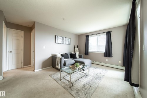 Living area featuring neutral wall tones, carpet flooring, baseboard heating, a white-framed window, and white interior doors - 115 4309 33 Street, Stony Plain, AB 