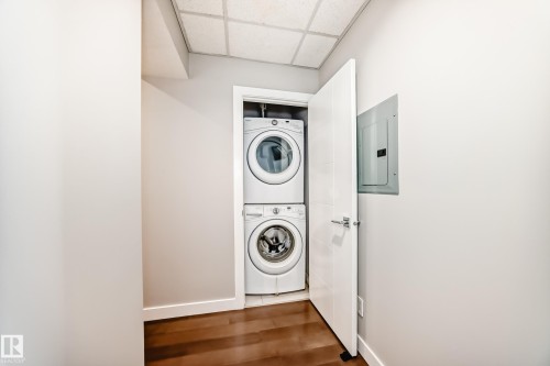 Dedicated laundry closet featuring a stacked washer and dryer, wood-finish flooring, and a contemporary white door with a polished chrome handle - 2604 10238 103 Street, Edmonton, AB 