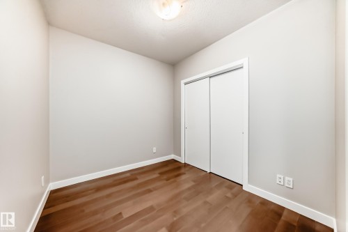 Room featuring warm wood-finish flooring, light neutral-toned walls, and bright white baseboards - 2604 10238 103 Street, Edmonton, AB 