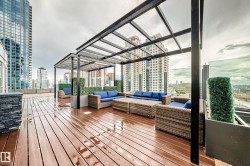 Expansive rooftop deck featuring wood-finish flooring, multiple black metal pergolas, and glass panel railings - 