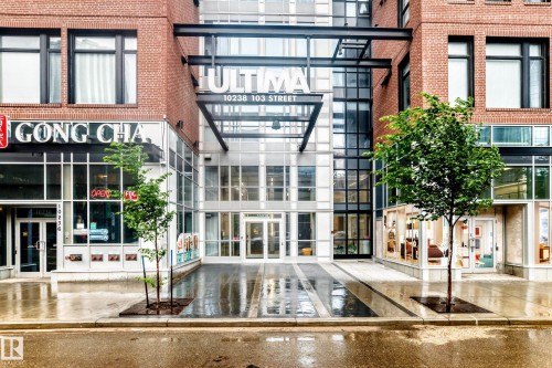 Modern building entry featuring a glass facade, brick exterior, metal architectural accents, a prominent building sign, and a paved walkway - 2604 10238 103 Street, Edmonton, AB 