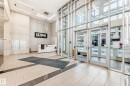 Modern lobby featuring a light-toned tile floor with dark accent banding, a white reception desk, contemporary suspended lighting, and a prominent building sign - 2604 10238 103 Street, Edmonton, AB 
