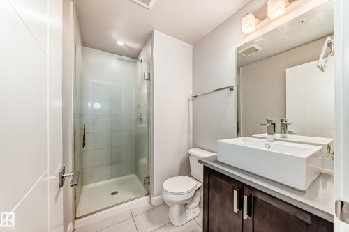 Modern bathroom featuring a glass-enclosed shower with tile surround, a dark wood-finish vanity with a light countertop, and a vessel sink with a contemporary faucet - 2604 10238 103 Street, Edmonton, AB 