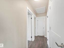 Hallway featuring wood-finish flooring, light-toned walls, multiple paneled doors, and a ceiling-mounted light fixture - 