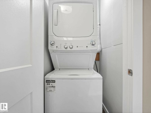 Dedicated laundry closet featuring a white stacked washer and dryer unit, white walls, and a light-colored door with a brushed nickel handle - 12241 54 Street, Edmonton, AB 
