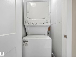 Dedicated laundry closet featuring a white stacked washer and dryer unit, white walls, and a light-colored door with a brushed nickel handle - 