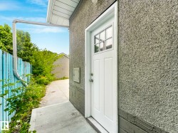 Side exterior entry featuring a white paneled door with windowpanes, stucco siding, and a concrete pathway - 