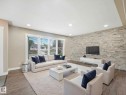 Spacious living area featuring a stacked stone accent wall, wood-finish flooring, and recessed ceiling lighting - 12241 54 Street, Edmonton, AB 