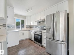 Modern kitchen featuring white cabinetry, stainless steel appliances, light-toned countertops, a mosaic tile backsplash, and wood-finish flooring - 