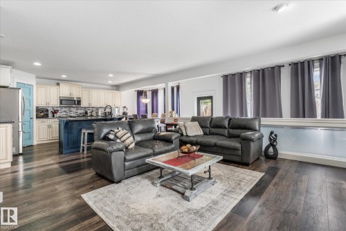 Open-concept living space featuring wood-finish flooring, a kitchen with a blue island and light-toned cabinetry, a subway tile backsplash, stainless steel appliances, and recessed lighting - 18 Woodbend Way, Fort Saskatchewan, AB 