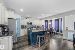 Kitchen featuring a central island with seating, dark countertops, white cabinetry, stainless steel appliances, and wood-finish flooring - 