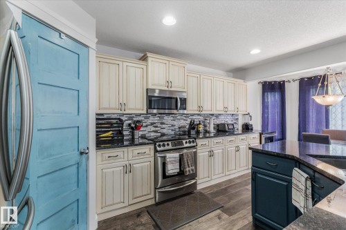Spacious kitchen featuring cream-colored cabinetry, a mosaic tile backsplash, black countertops, and wood-finish flooring - 18 Woodbend Way, Fort Saskatchewan, AB 