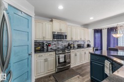 Spacious kitchen featuring cream-colored cabinetry, a mosaic tile backsplash, black countertops, and wood-finish flooring - 