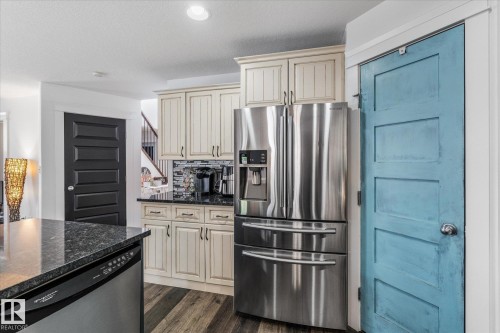 Kitchen featuring stainless steel appliances, light-toned cabinetry, dark countertops, and wood-finish flooring - 18 Woodbend Way, Fort Saskatchewan, AB 