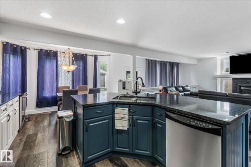 Kitchen island featuring a stainless steel dishwasher, dark countertop, and integrated sink with a pulldown faucet - 18 Woodbend Way, Fort Saskatchewan, AB 