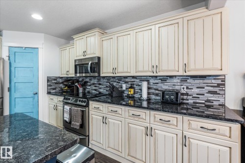 Kitchen featuring light-toned cabinetry with dark hardware, dark granite countertops, and a gray-toned mosaic tile backsplash - 18 Woodbend Way, Fort Saskatchewan, AB 