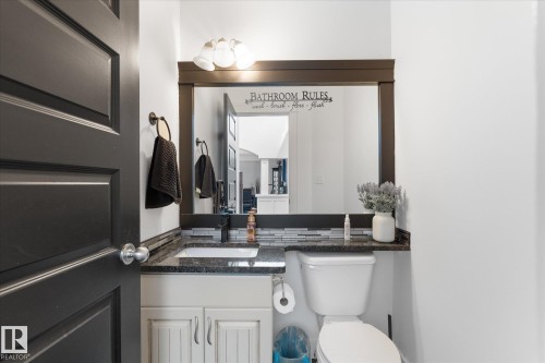 Bathroom featuring a dark wood-framed mirror with integrated lighting, a granite countertop, a rectangular undermount sink, and a black faucet - 18 Woodbend Way, Fort Saskatchewan, AB 