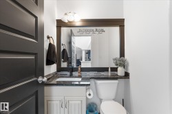 Bathroom featuring a dark wood-framed mirror with integrated lighting, a granite countertop, a rectangular undermount sink, and a black faucet - 