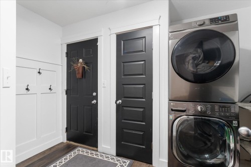 Laundry area featuring stacked front-loading appliances, dark wood-finish flooring, and white trim accents - 18 Woodbend Way, Fort Saskatchewan, AB 
