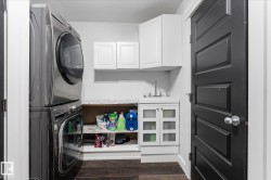 Dedicated laundry area featuring stacked appliances, a utility sink with a vanity, upper and lower cabinetry, wood-finish flooring, and a paneled interior door - 