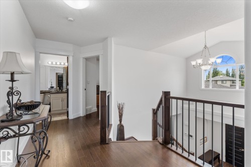 Upper-level hallway featuring wood-finish flooring, a wrought iron and wood railing, arched window, and a chandelier - 18 Woodbend Way, Fort Saskatchewan, AB 
