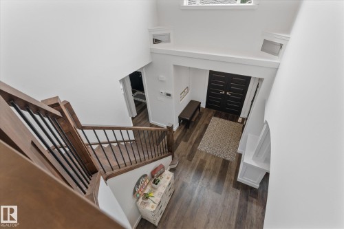 Two-story foyer featuring wood-finish flooring, a dark wood staircase with black metal balusters, and a black double-door entry - 18 Woodbend Way, Fort Saskatchewan, AB 