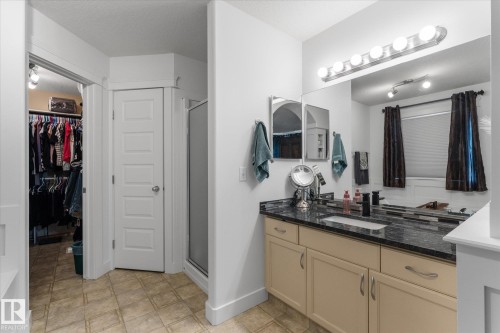 Bathroom featuring a double vanity with stone countertops, a large frameless mirror, and neutral-toned cabinetry - 18 Woodbend Way, Fort Saskatchewan, AB 
