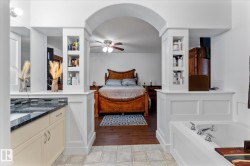 Arched entryway connecting spaces, featuring built-in shelving, a deep soaking tub with chrome fixtures, a vanity with a dark speckled countertop, and light-toned cabinetry - 