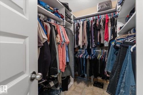 Walk-in closet featuring built-in shelving, multiple hanging rods, and neutral-toned flooring - 18 Woodbend Way, Fort Saskatchewan, AB 