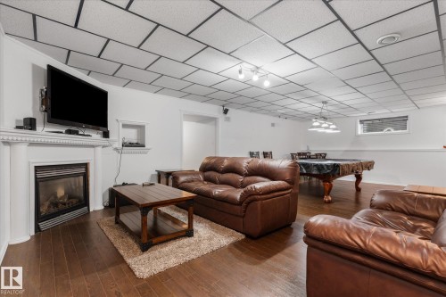 Recessed drop ceiling with integrated lighting, wood-finish flooring, built-in fireplace with white mantel, a wall niche, and an exposed window - 18 Woodbend Way, Fort Saskatchewan, AB 