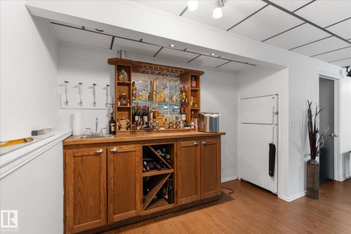 Built-in wet bar featuring wood cabinetry, integrated wine storage, a stainless steel sink, and track lighting - 18 Woodbend Way, Fort Saskatchewan, AB 