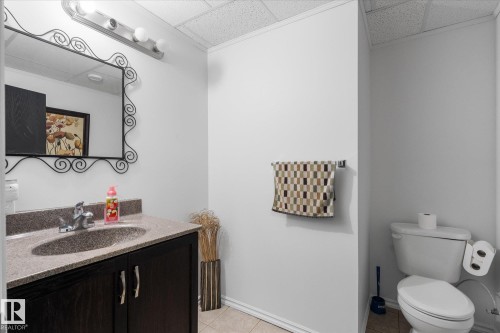 Vanity area featuring a dark wood-finish cabinet with silver-tone pulls, a built-in sink, and a light-toned countertop - 18 Woodbend Way, Fort Saskatchewan, AB 