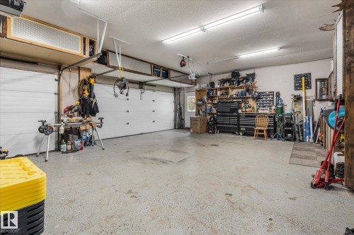 Spacious garage featuring two overhead doors, a speckled concrete floor, built-in shelving, abundant overhead lighting, and an integrated workbench area - 18 Woodbend Way, Fort Saskatchewan, AB 