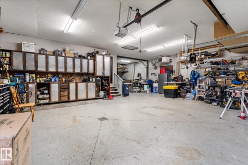 Expansive garage space featuring a concrete floor, extensive built-in cabinetry with wood-finish frames and textured panel inserts, and overhead fluorescent lighting fixtures - 18 Woodbend Way, Fort Saskatchewan, AB 