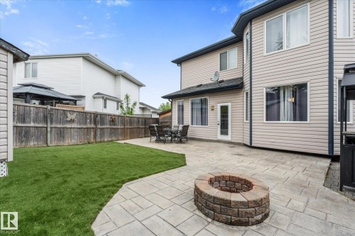 Expansive backyard featuring a stone paver patio, a built-in stone fire pit, and a manicured lawn - 18 Woodbend Way, Fort Saskatchewan, AB 