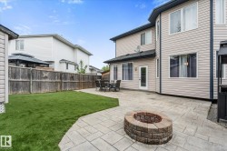 Expansive backyard featuring a stone paver patio, a built-in stone fire pit, and a manicured lawn - 