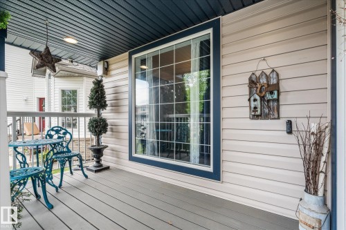 Covered front porch featuring neutral vinyl siding, a large multi-pane window with dark trim, gray composite decking, and a dark blue beadboard ceiling - 18 Woodbend Way, Fort Saskatchewan, AB 