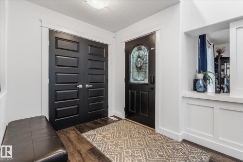 Entryway featuring dark wood-finish flooring, a decorative area rug, and a solid black entry door with leaded glass insert - 18 Woodbend Way, Fort Saskatchewan, AB 