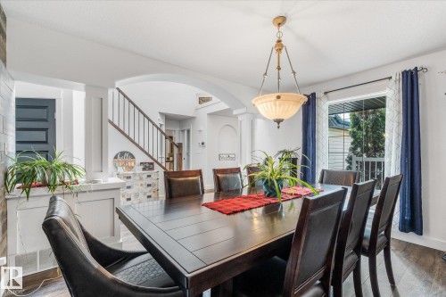 Spacious dining area featuring dark wood-finish flooring, a contemporary chandelier, and a large window - 18 Woodbend Way, Fort Saskatchewan, AB 